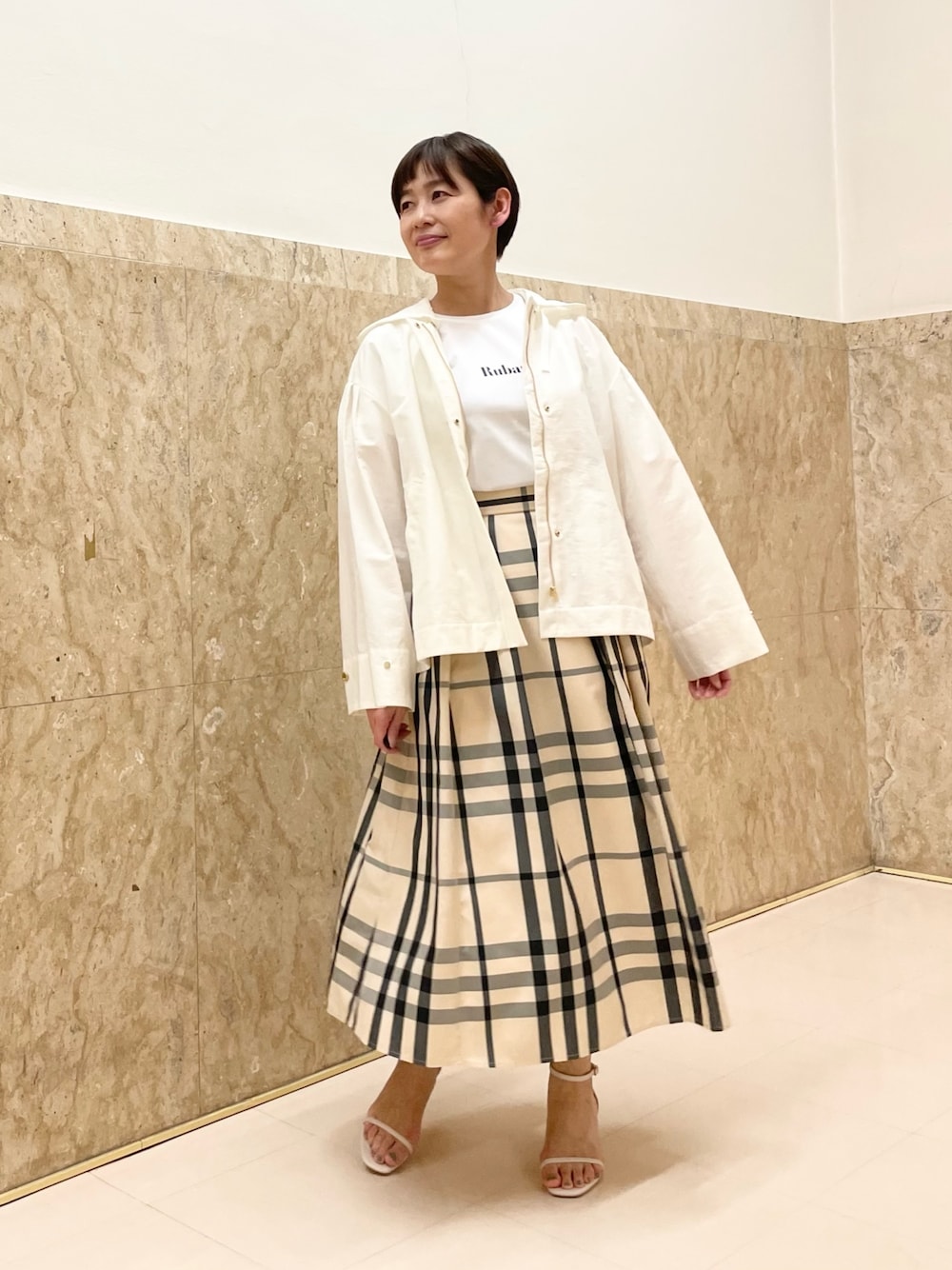 ホワイト系のサンダル、ベージュ系のスカート、ホワイト系のマウンテンパーカーを着用したレディースの春コーディネートの1枚目の写真