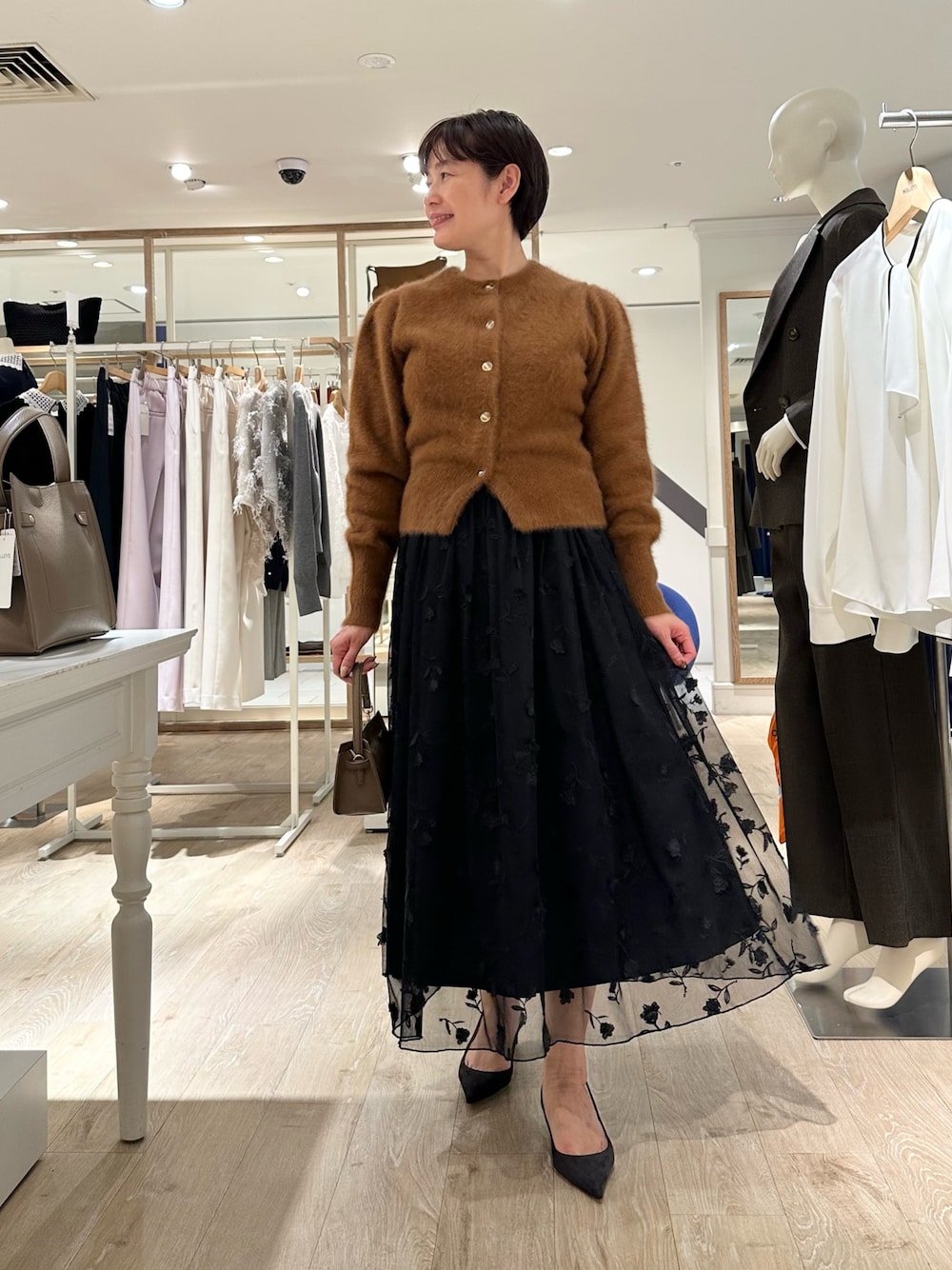 ブラウン系のカーディガン/ボレロ、ブラック系のスカート、ベージュ系のショルダーバッグを着用したレディースの秋コーディネートの1枚目の写真