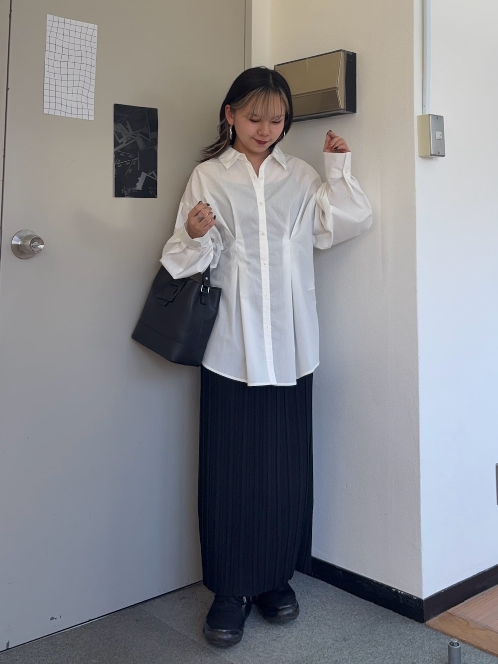 ブラック系のスカート、ブラック系のショルダーバッグ、ホワイト系のシャツ/ブラウスを着用したレディースの春コーディネートの1枚目の写真