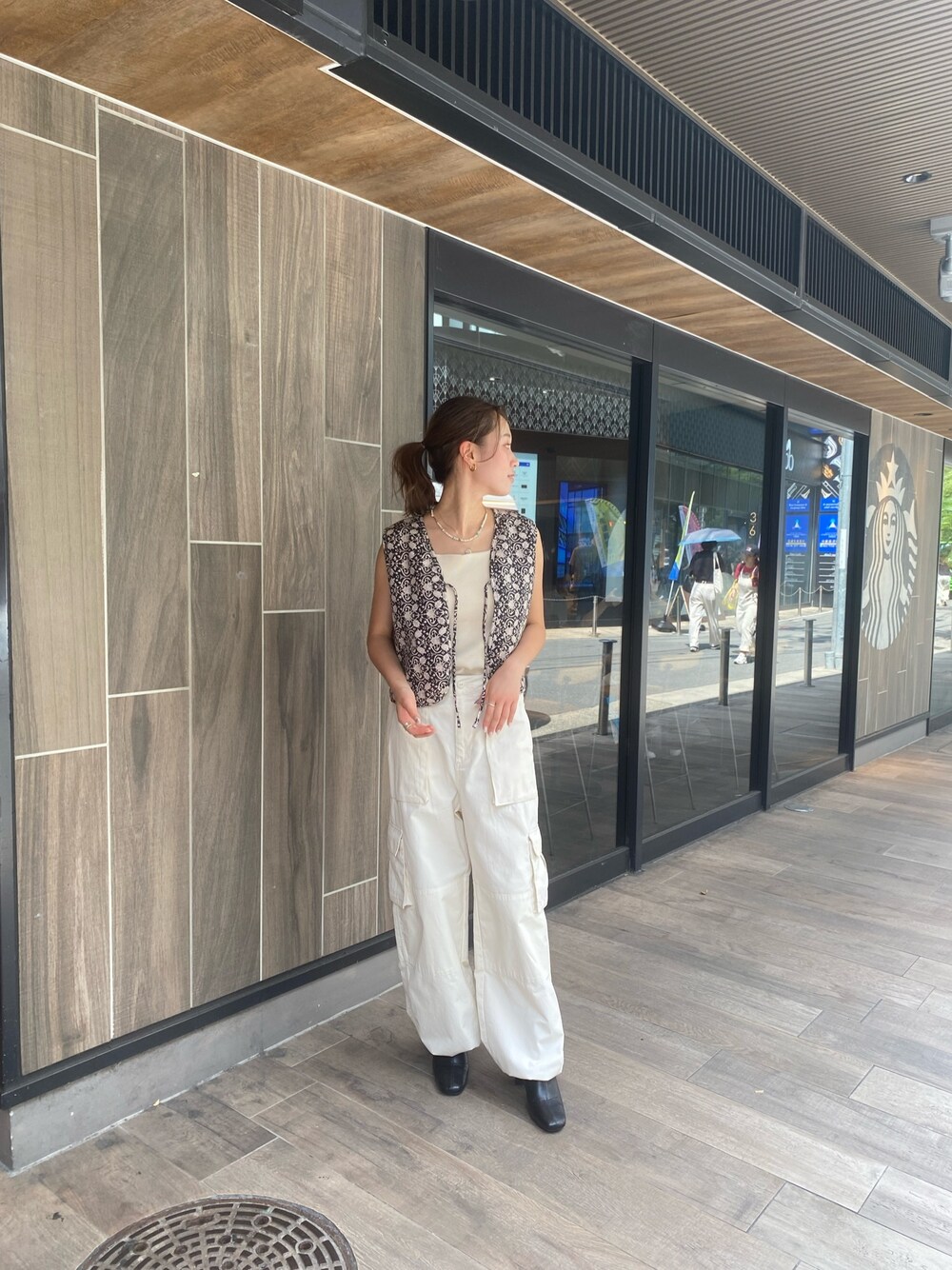 ホワイト系のカーゴパンツ、ブラック系のベスト、ホワイト系のキャミソールを着用したレディースの夏コーディネートの1枚目の写真