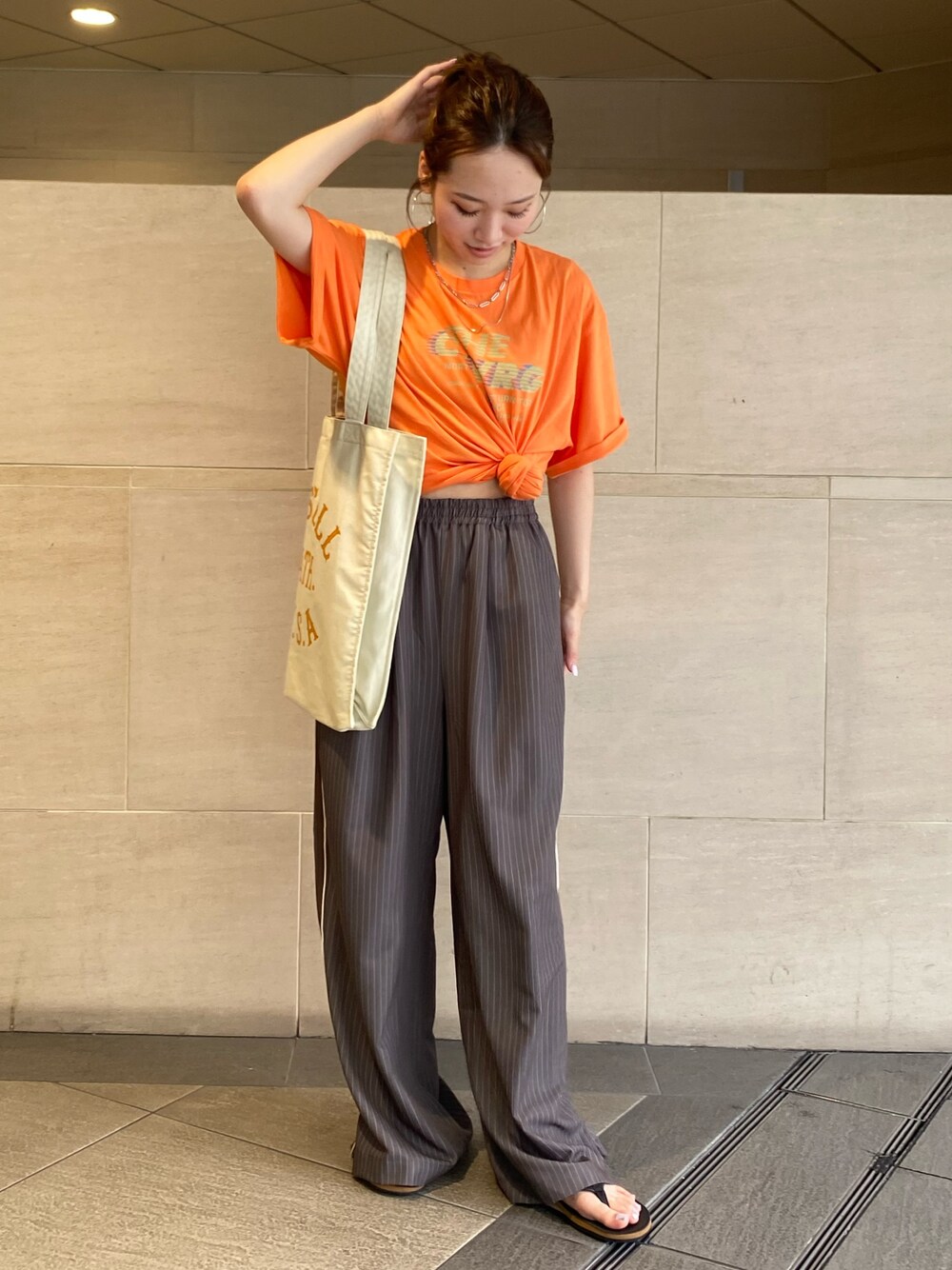 グレー系のその他パンツ、オレンジ系のTシャツ/カットソー、ホワイト系のトートバッグを着用したレディースの夏コーディネートの1枚目の写真