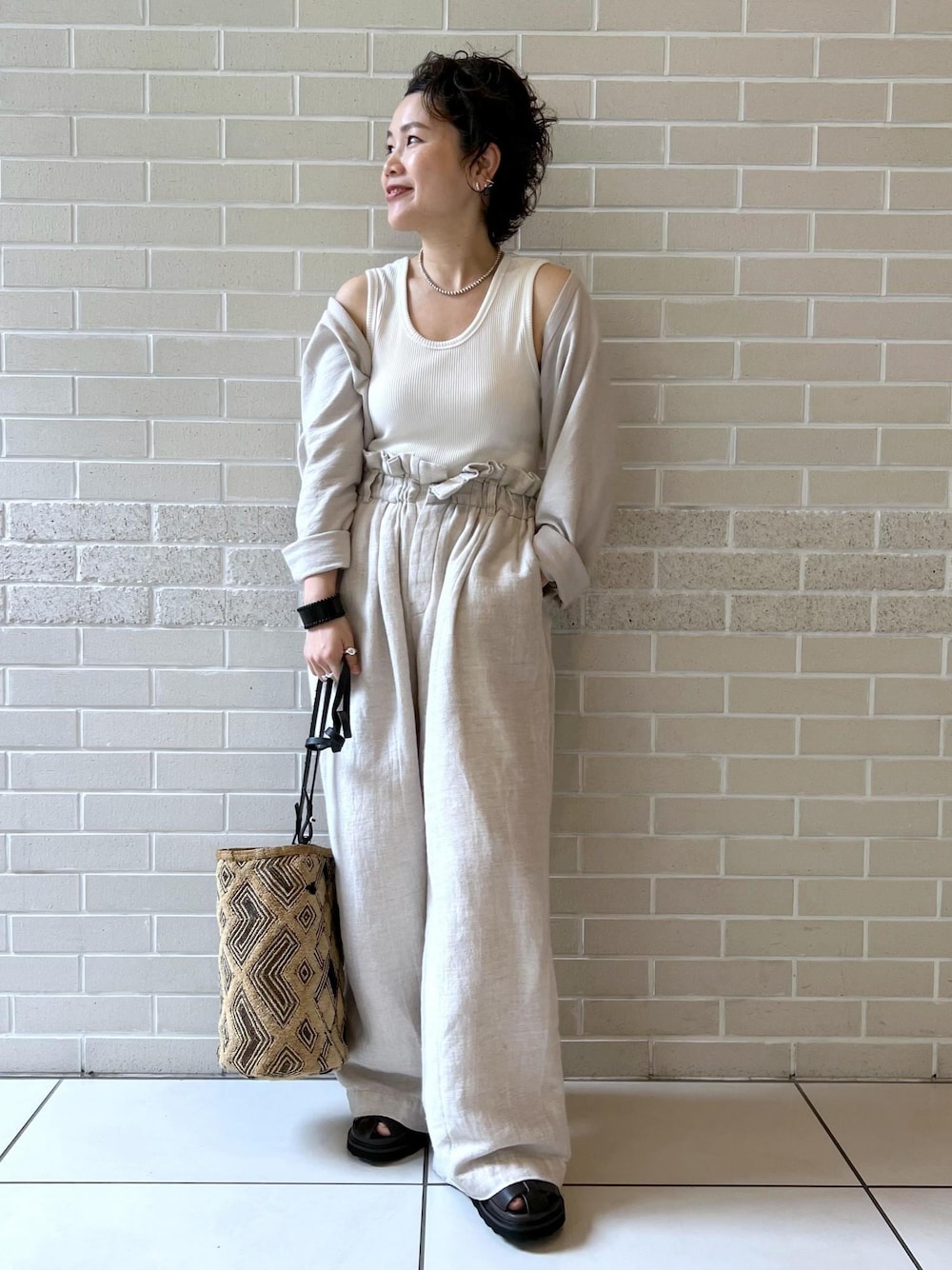 ブラウン系のサンダル、ホワイト系のカーディガン/ボレロ、ホワイト系のスラックスを着用したレディースの夏コーディネートの1枚目の写真