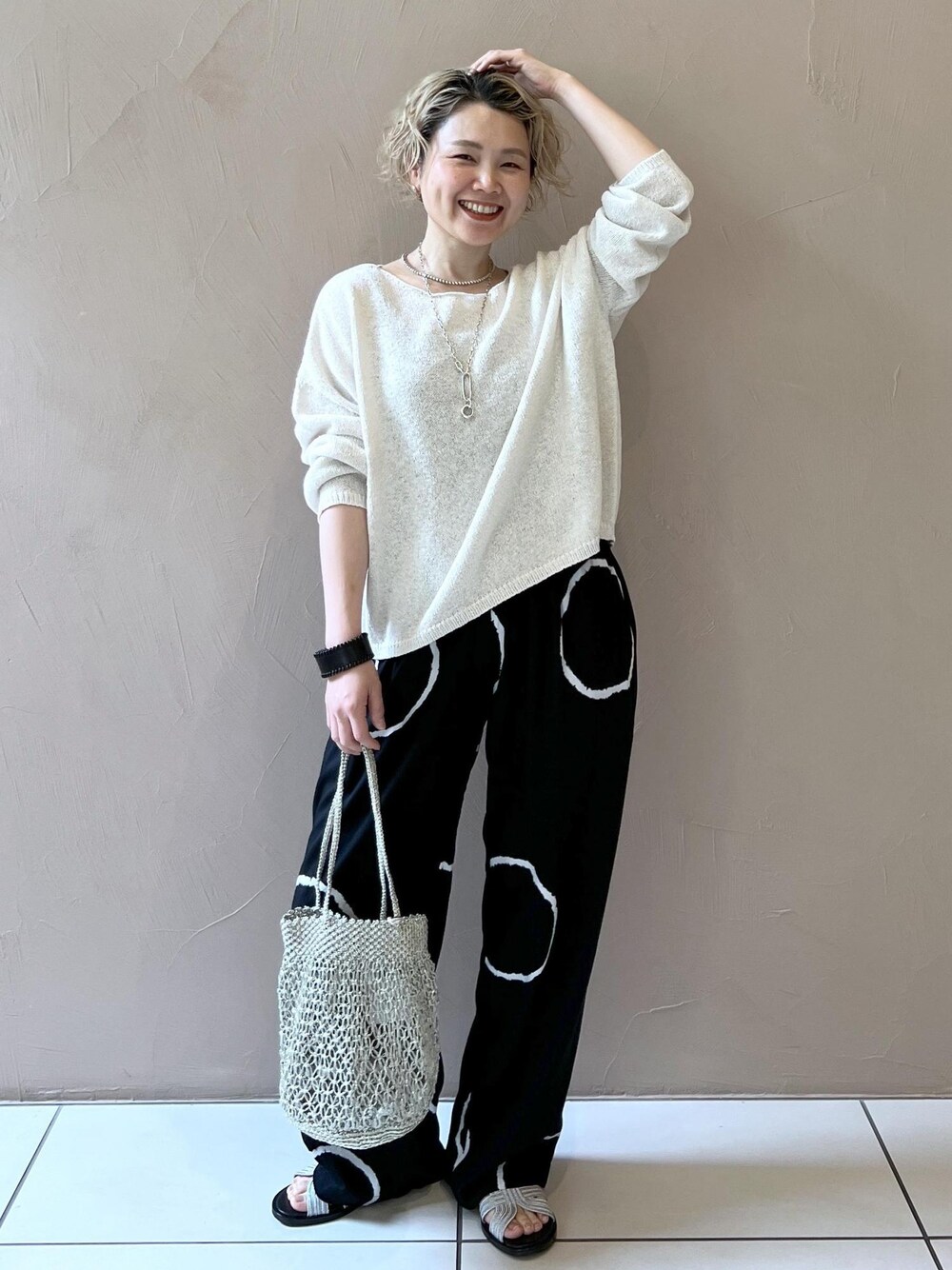 ゴールド系のハンドバッグ、シルバー系のサンダル、ホワイト系のニット/セーターを着用したレディースの春コーディネートの1枚目の写真