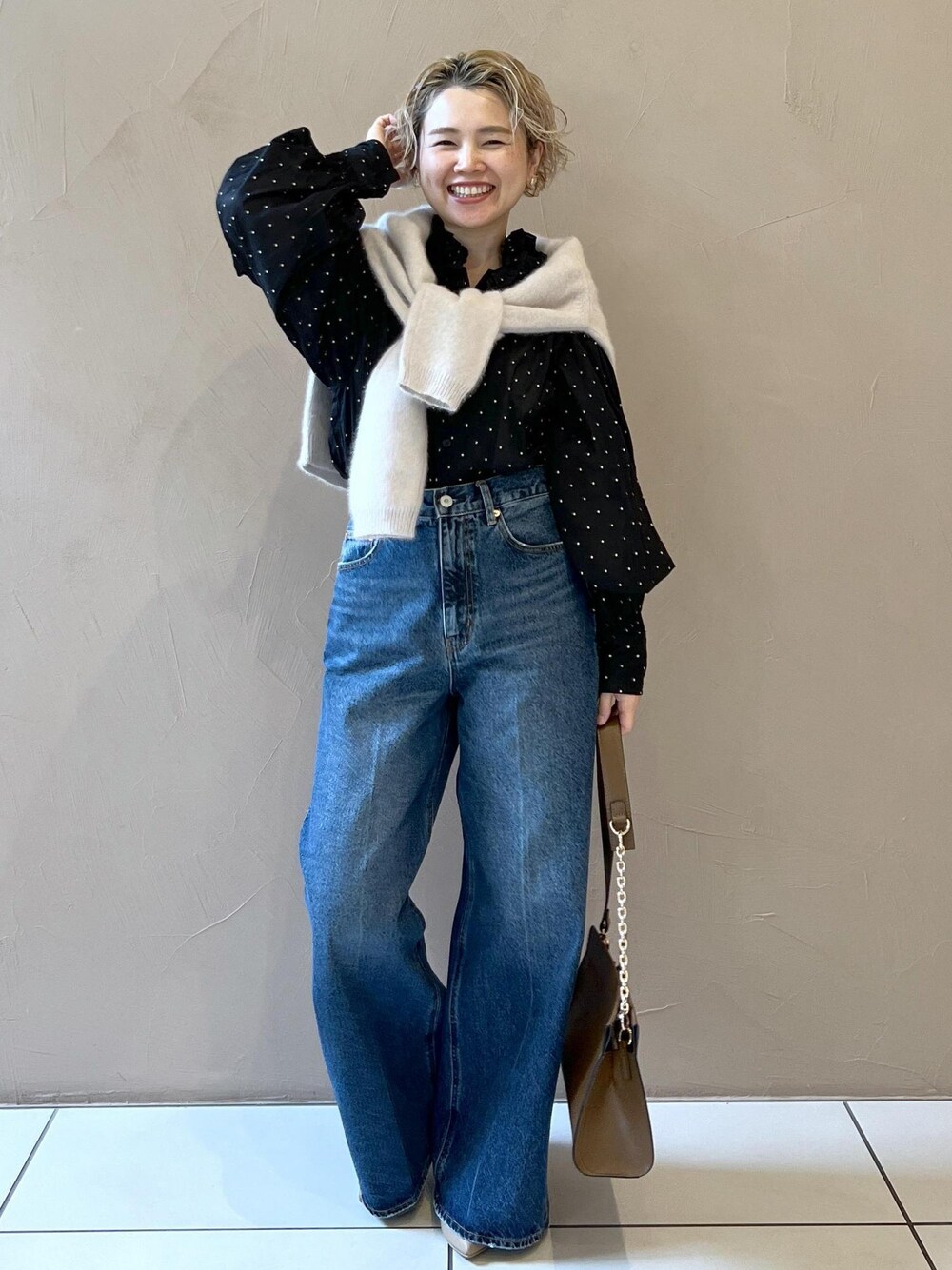 グレー系のニット/セーター、ブルー系のデニムパンツ、ブラウン系のショルダーバッグを着用したレディースの秋コーディネートの1枚目の写真