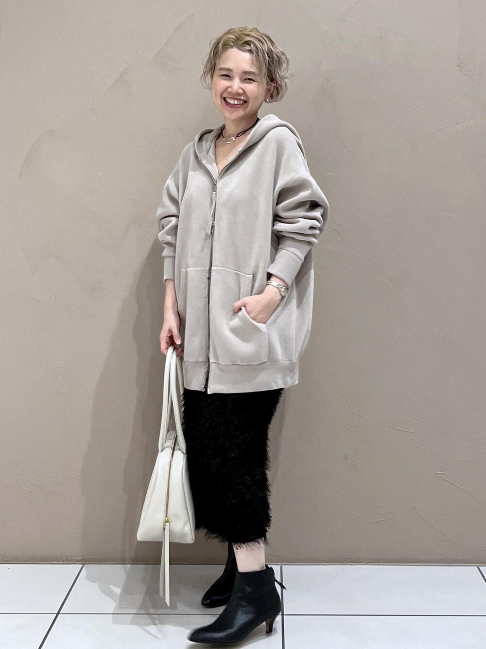 ベージュ系のパーカー、ホワイト系のボストンバッグ、ブラック系のブーツを着用したレディースの秋コーディネートの1枚目の写真