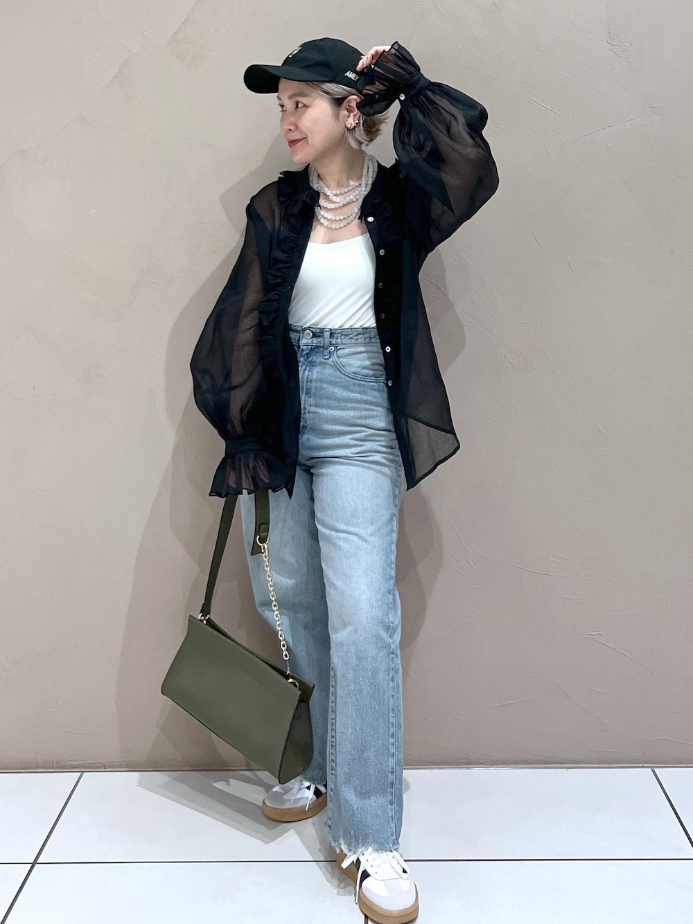 グリーン系のショルダーバッグ、ブルー系のデニムパンツ、ホワイト系のスニーカーを着用したレディースの夏コーディネートの1枚目の写真