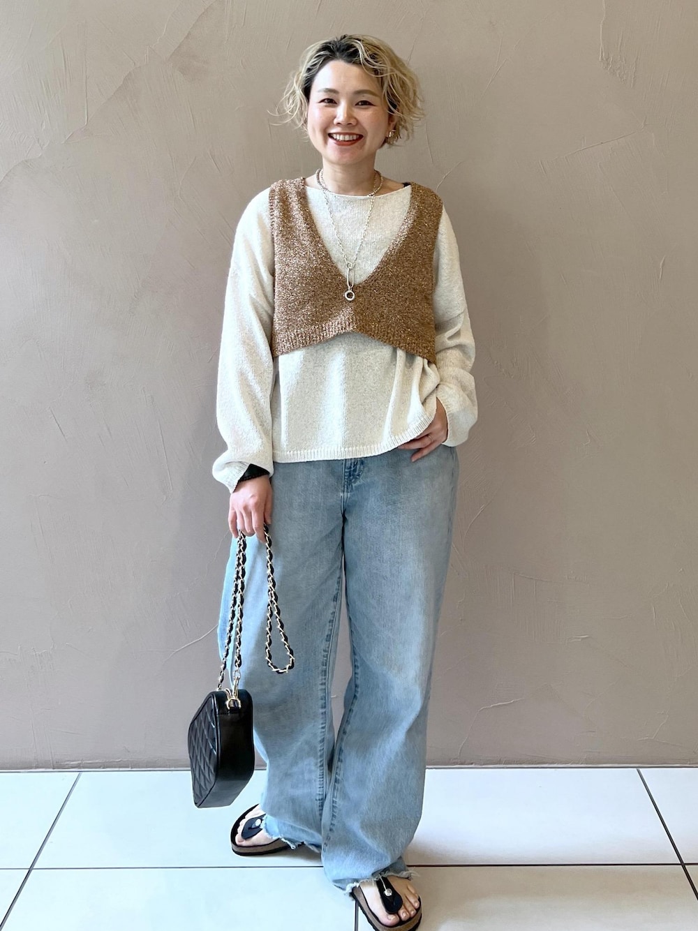 ブラック系のショルダーバッグ、ブルー系のデニムパンツ、ホワイト系のニット/セーターを着用したレディースの春コーディネートの1枚目の写真