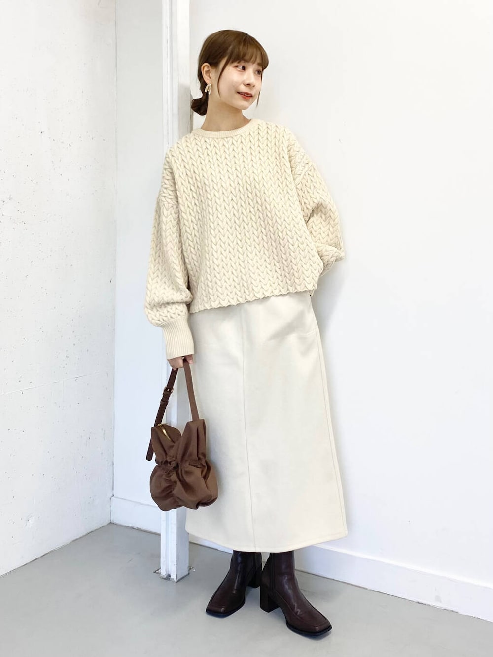 ブラウン系のハンドバッグ、ブラウン系のブーツ、ホワイト系のスカートを着用したレディースの冬コーディネートの1枚目の写真