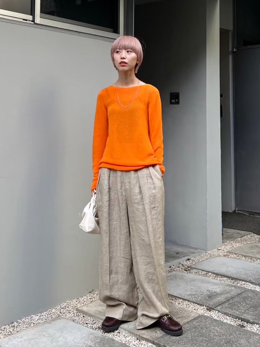 オレンジ系のニット/セーター、ベージュ系のスラックス、ホワイト系のショルダーバッグを着用したレディースの冬コーディネートの1枚目の写真