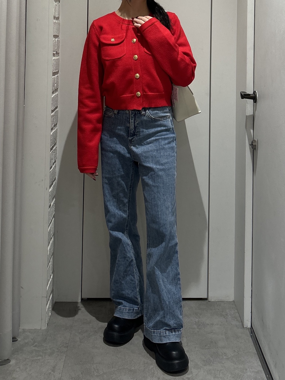 レッド系のニット/セーター、ブルー系のデニムパンツ、ホワイト系のショルダーバッグを着用したレディースの秋コーディネートの1枚目の写真