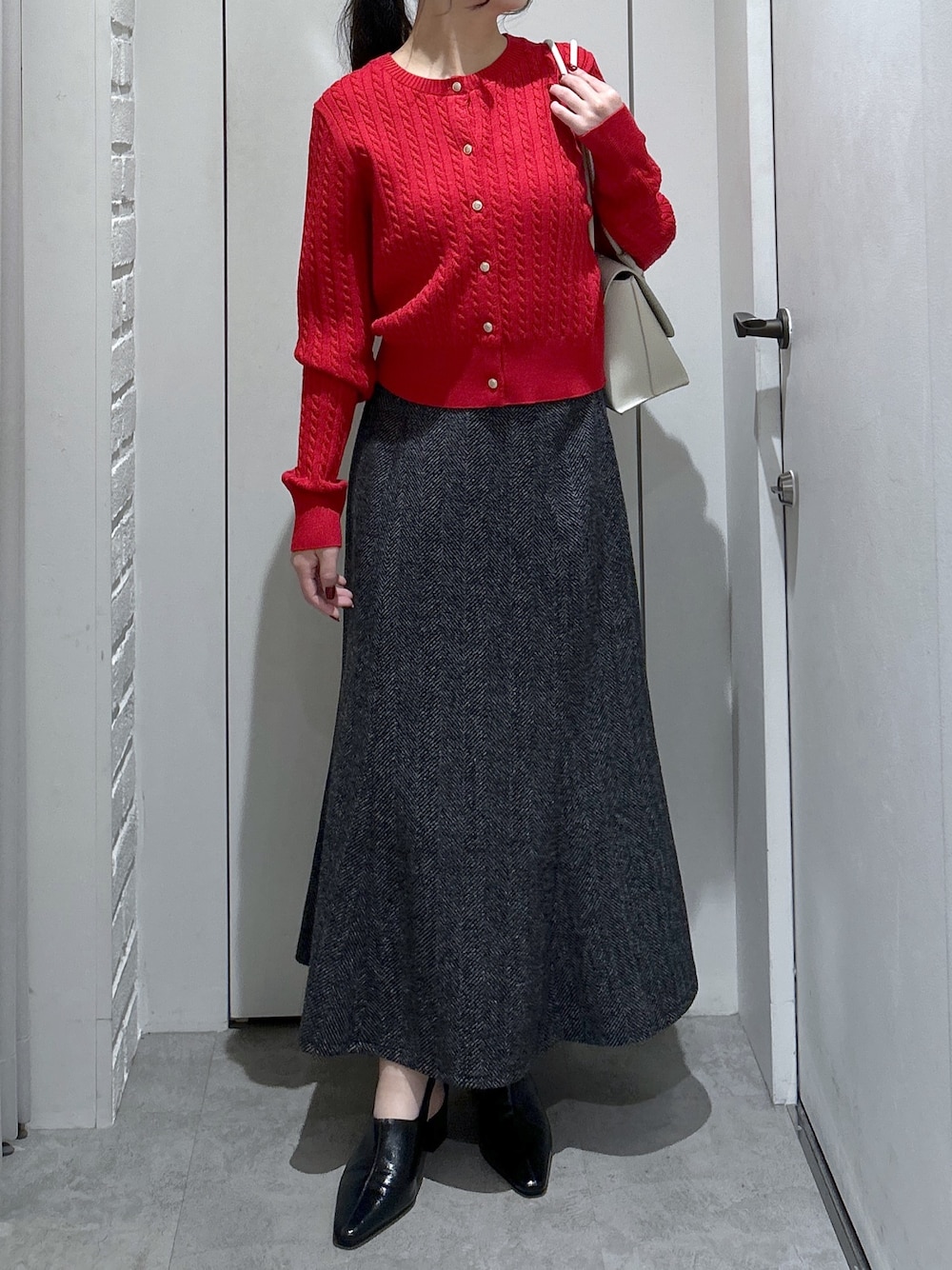 ブラック系のスカート、ホワイト系のショルダーバッグ、レッド系のニット/セーターを着用したレディースの冬コーディネートの1枚目の写真