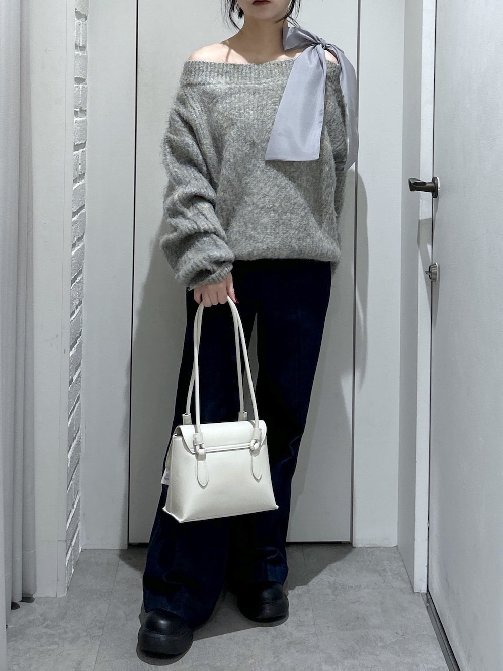グレー系のニット/セーター、ブルー系のデニムパンツ、ホワイト系のショルダーバッグを着用したレディースの冬コーディネートの1枚目の写真