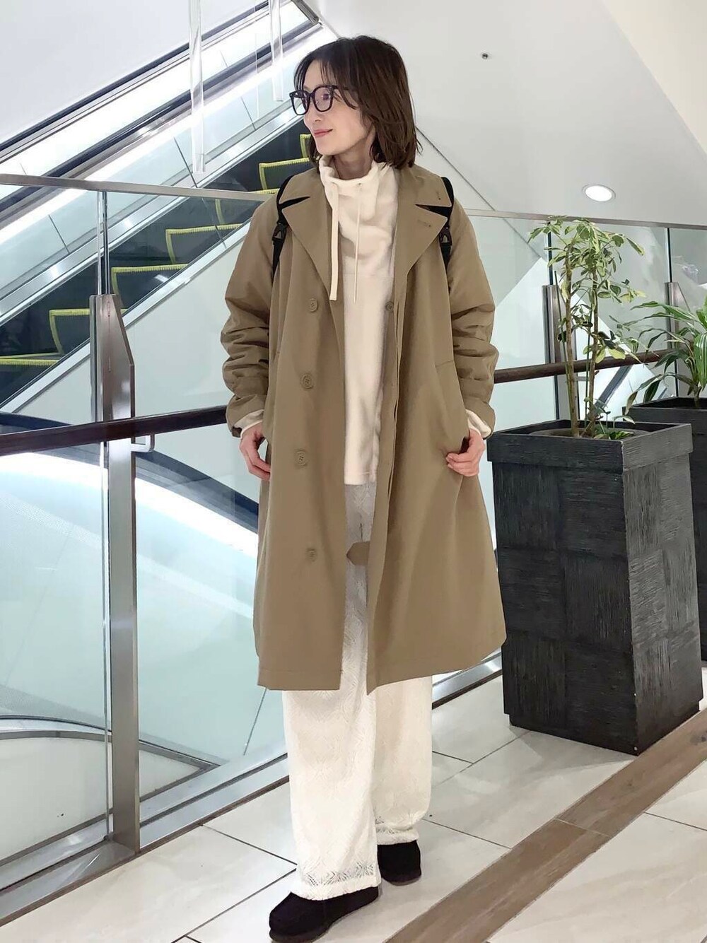 ブラウン系のステンカラーコート、ホワイト系のその他パンツ、ホワイト系のその他トップスを着用したレディースの冬コーディネートの1枚目の写真