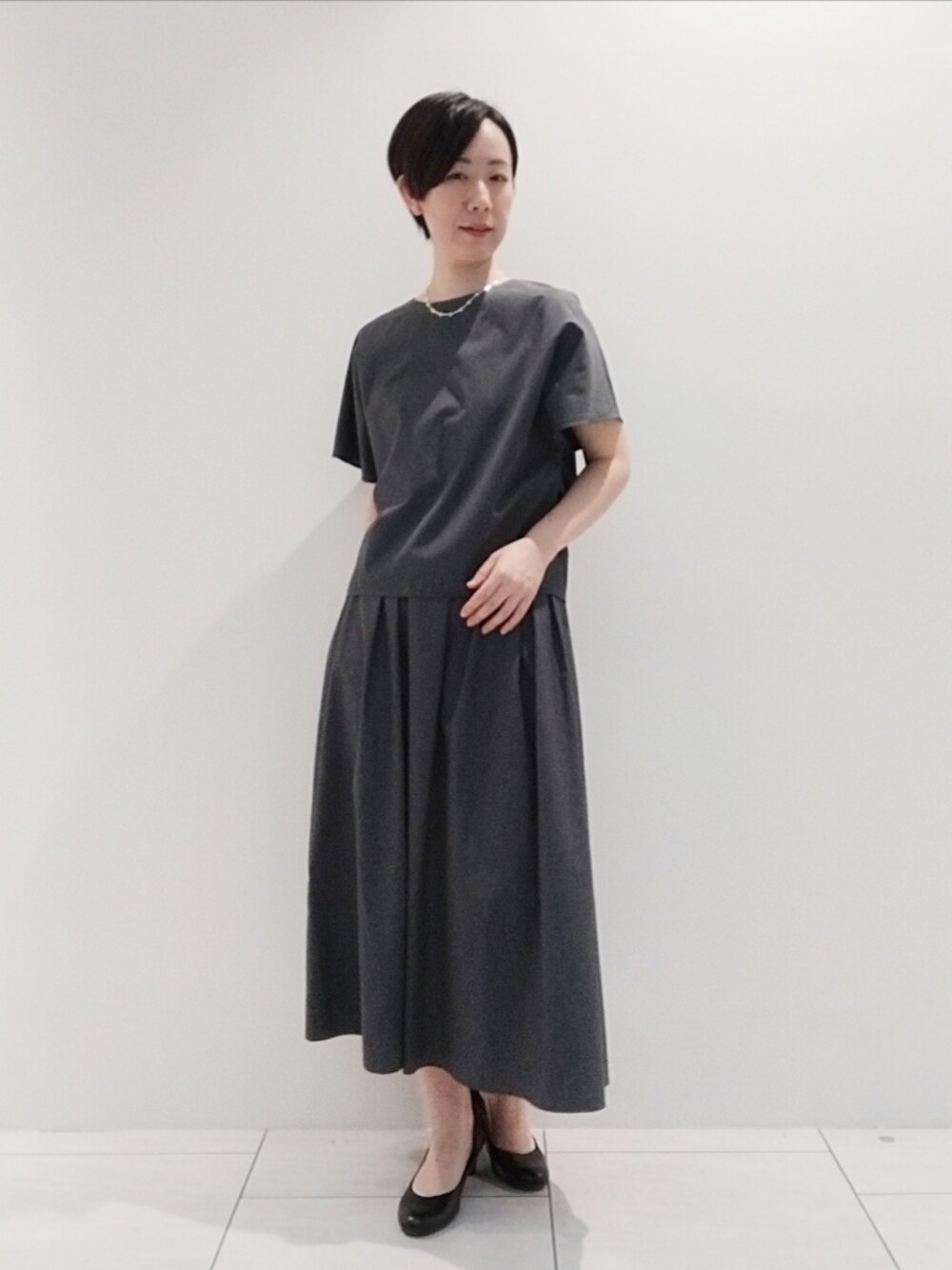 グレー系のシャツ/ブラウス、グレー系のスカート、シルバー系のネックレスを着用したレディースの夏コーディネートの1枚目の写真