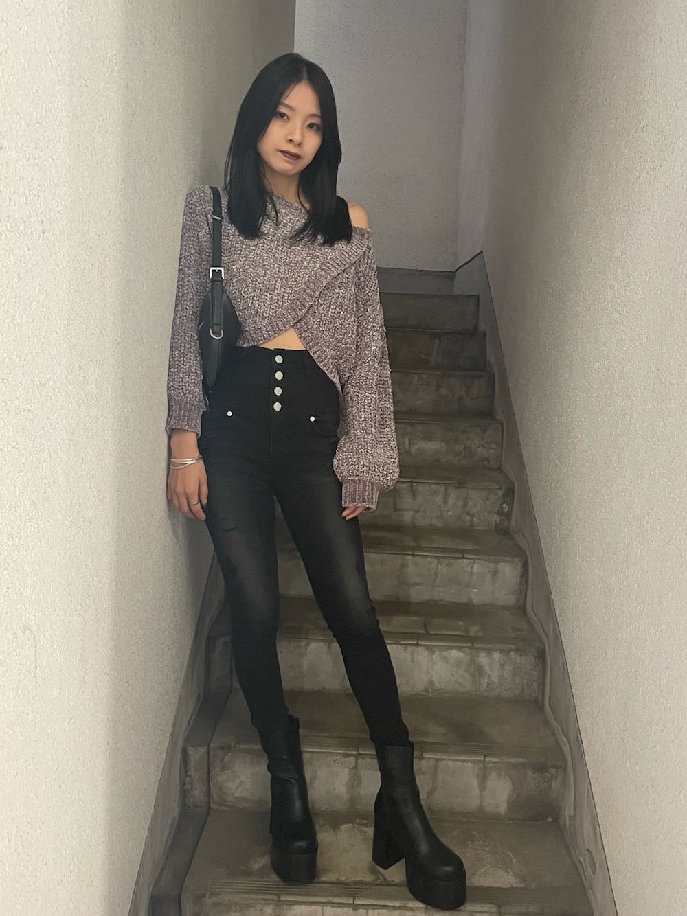 グレー系のニット/セーター、ブラック系のハンドバッグ、ブラック系のデニムパンツを着用したレディースの冬コーディネートの1枚目の写真