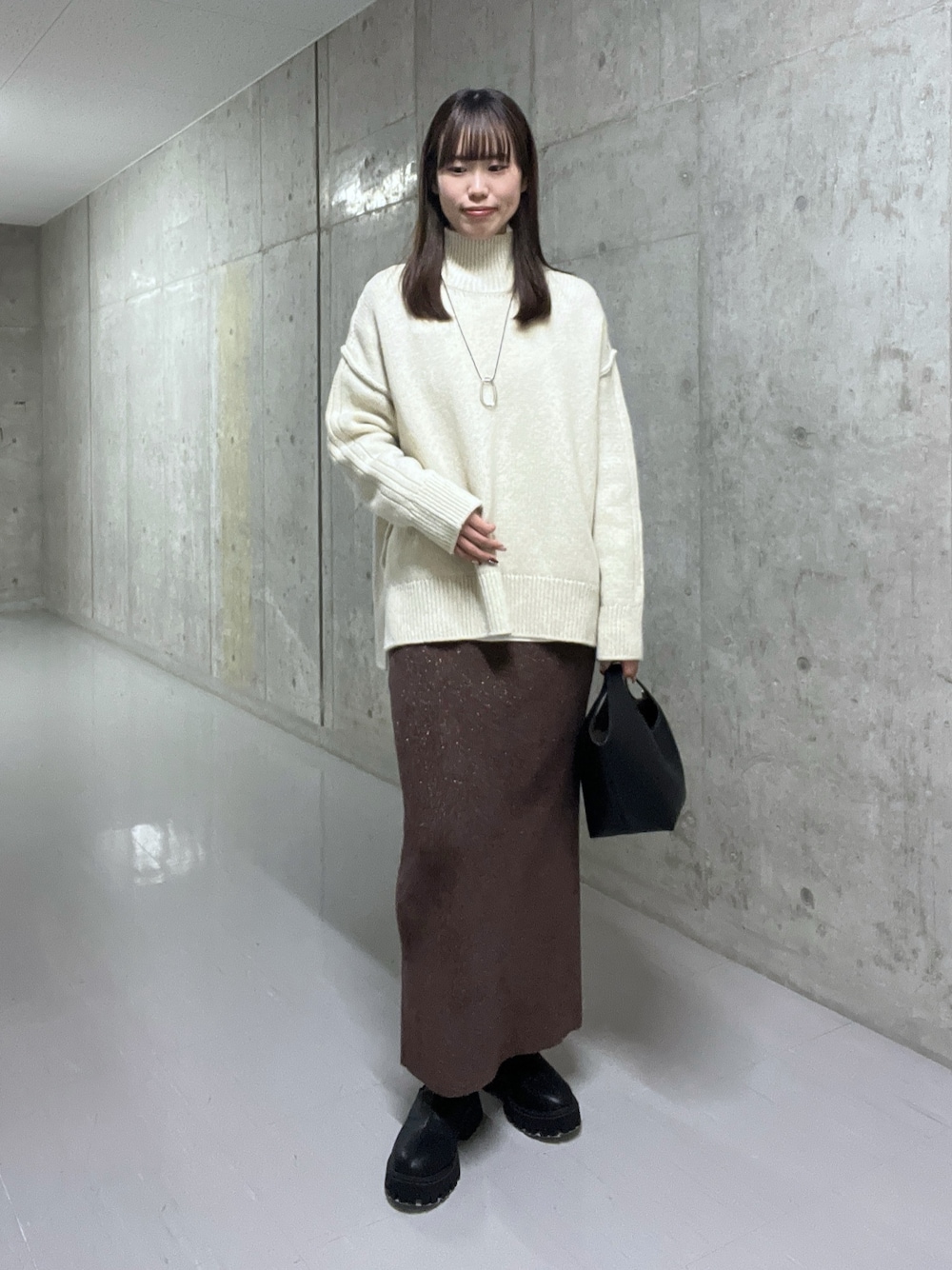 ホワイト系のニット/セーター、ブラウン系のスカート、ブラック系のブーツを着用したレディースの秋コーディネートの1枚目の写真