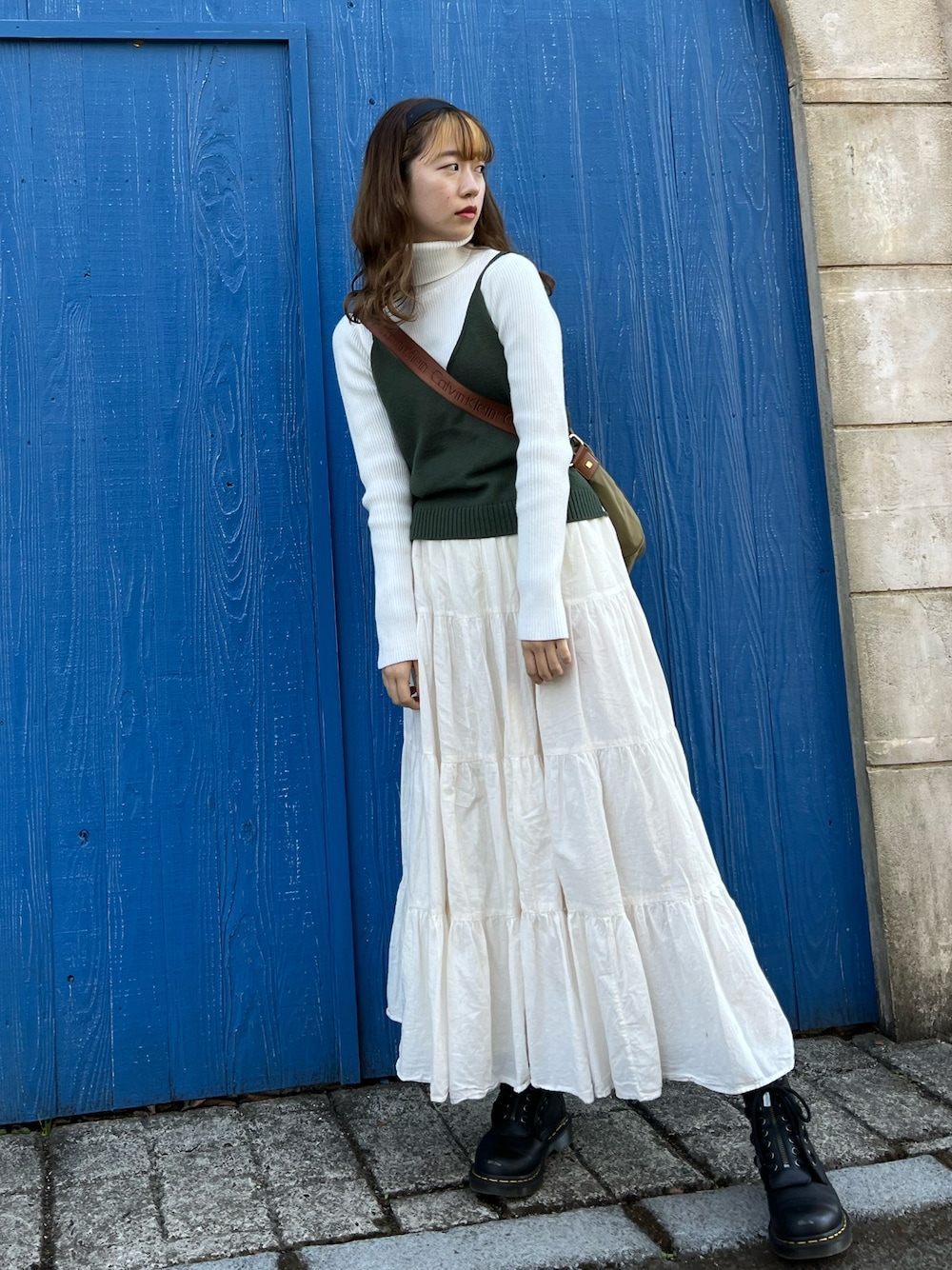 ホワイト系のスカート、ブラック系のブーツ、グリーン系のキャミソールを着用したレディースの春コーディネートの1枚目の写真
