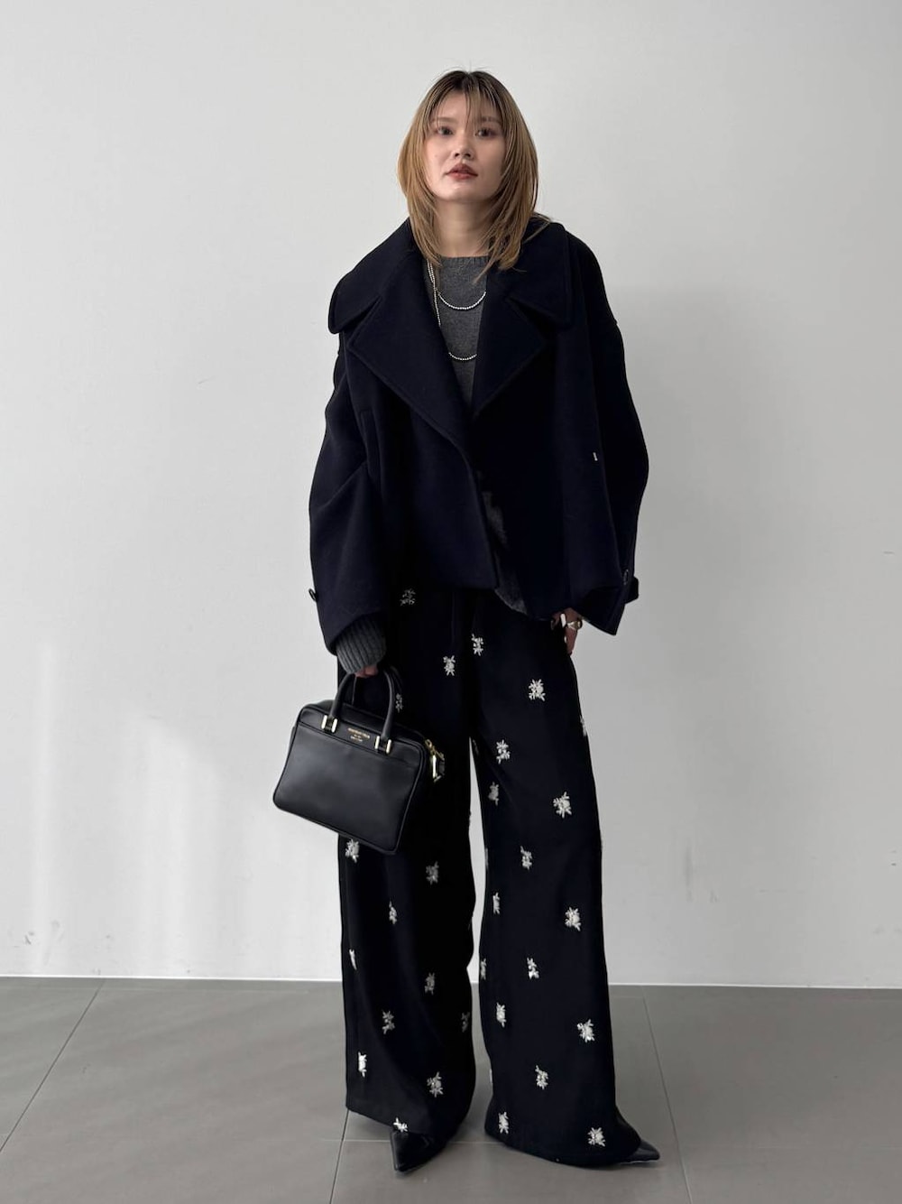 グレー系のニット/セーター、ブラック系のボストンバッグ、ブルー系のピーコートを着用したレディースの秋コーディネートの1枚目の写真