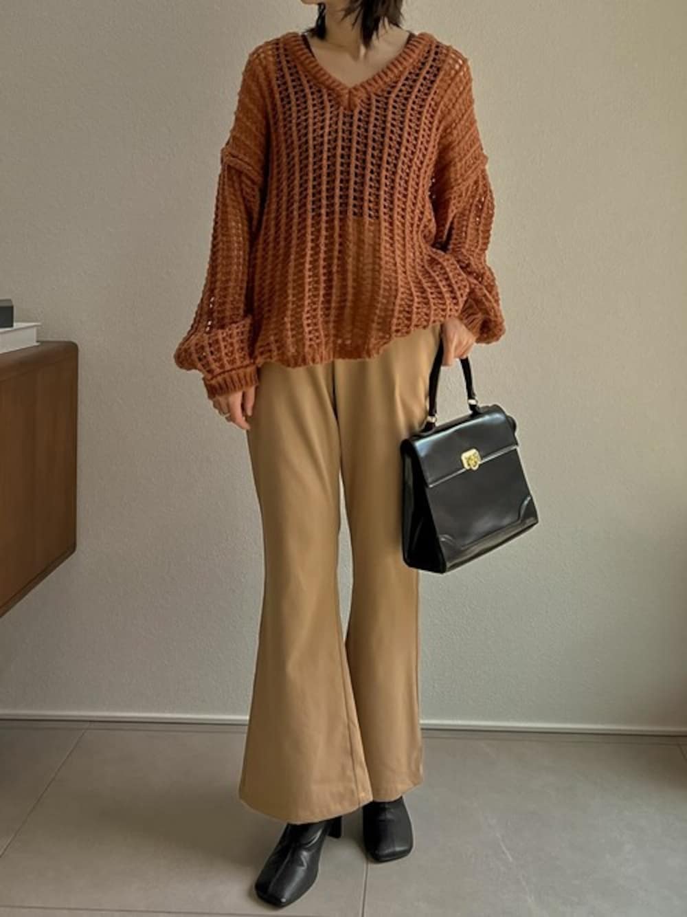 オレンジ系のニット/セーター、ベージュ系のその他パンツ、ブラック系のブーツを着用したレディースの夏コーディネートの1枚目の写真