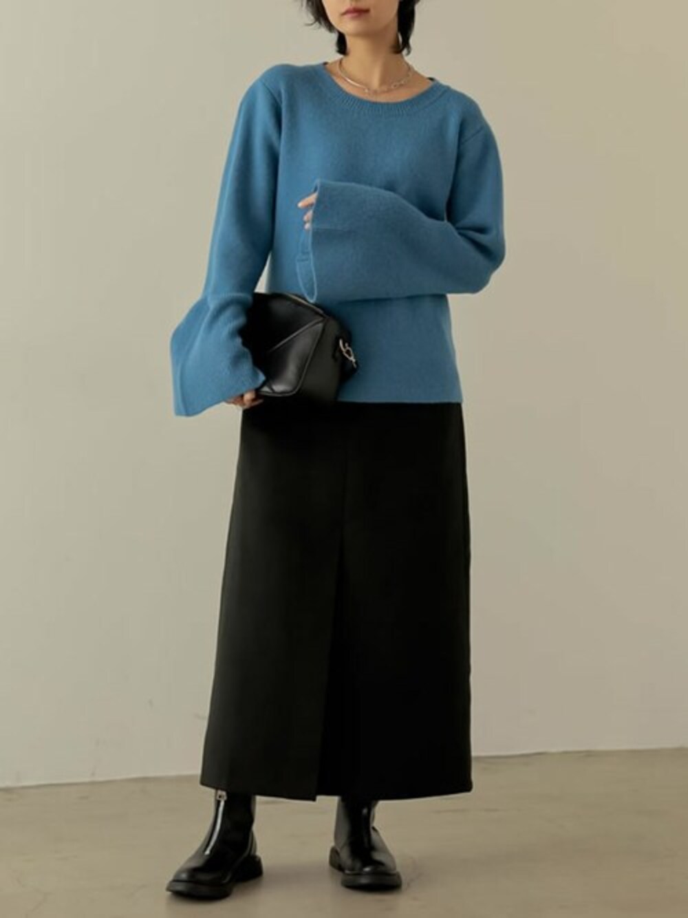 ブルー系のニット/セーター、ブラック系のスカート、ブラック系のショルダーバッグを着用したレディースの冬コーディネートの1枚目の写真