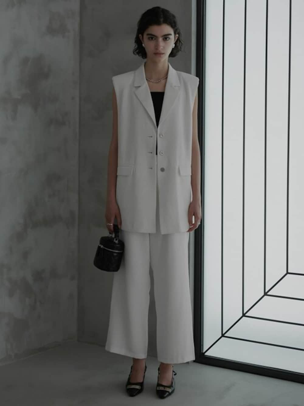 ホワイト系のベスト、ブラック系のキャミソール、ブラック系のパンプスを着用したレディースの夏コーディネートの1枚目の写真