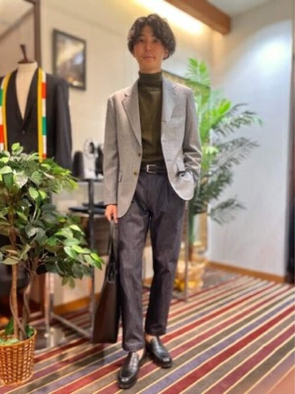 グレー系のテーラードジャケット、ブルー系のデニムパンツ、ブラック系のビジネスバッグを着用したメンズの秋コーディネートの1枚目の写真