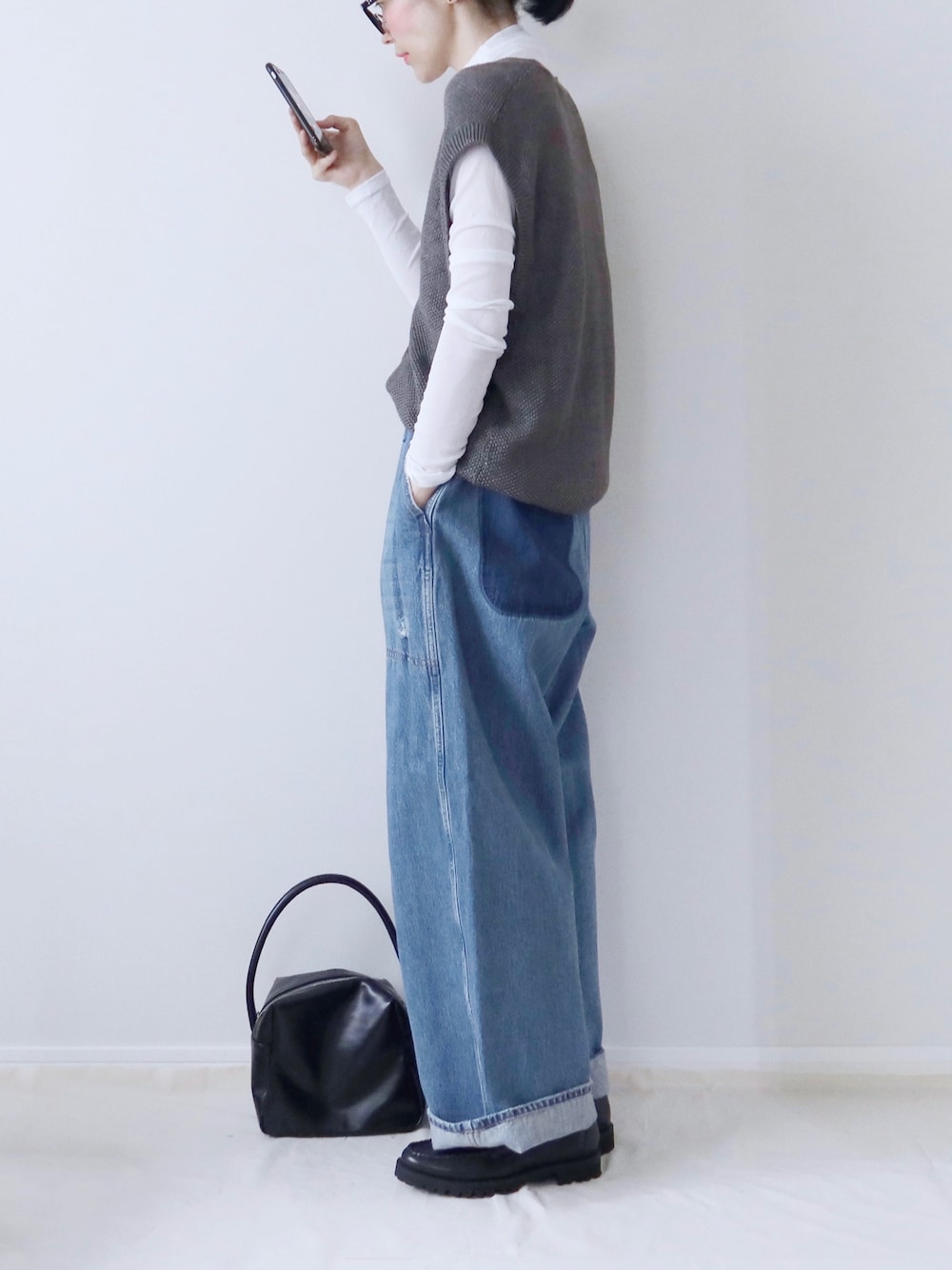 グレー系のニット/セーター、ホワイト系のTシャツ/カットソー、ブルー系のデニムパンツを着用したレディースの秋コーディネートの1枚目の写真