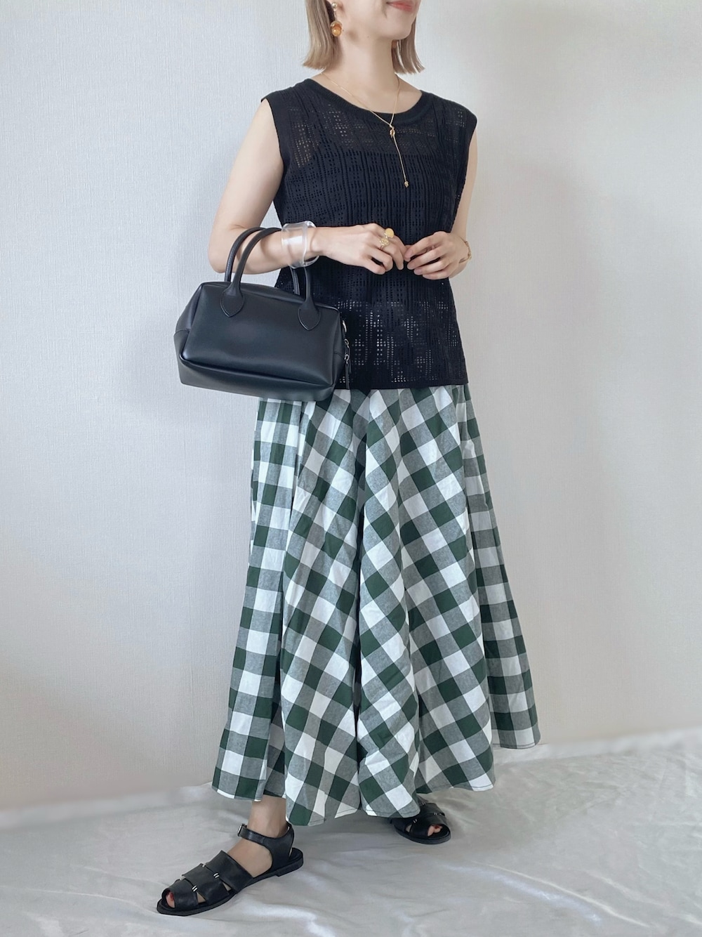 ブラック系のニット/セーター、ブラック系のバッグ、グリーン系のスカートを着用したレディースの春コーディネートの1枚目の写真