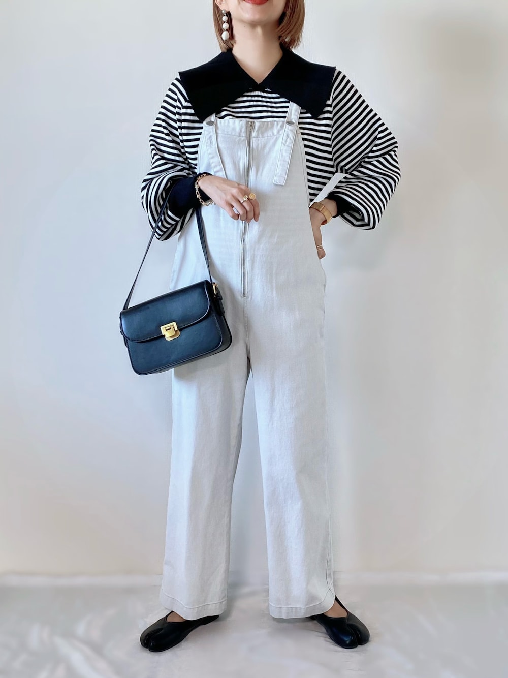 ブラック系のショルダーバッグ、ブラック系のニット/セーター、ホワイト系のサロペット/オーバーオールを着用したレディースの冬コーディネートの1枚目の写真