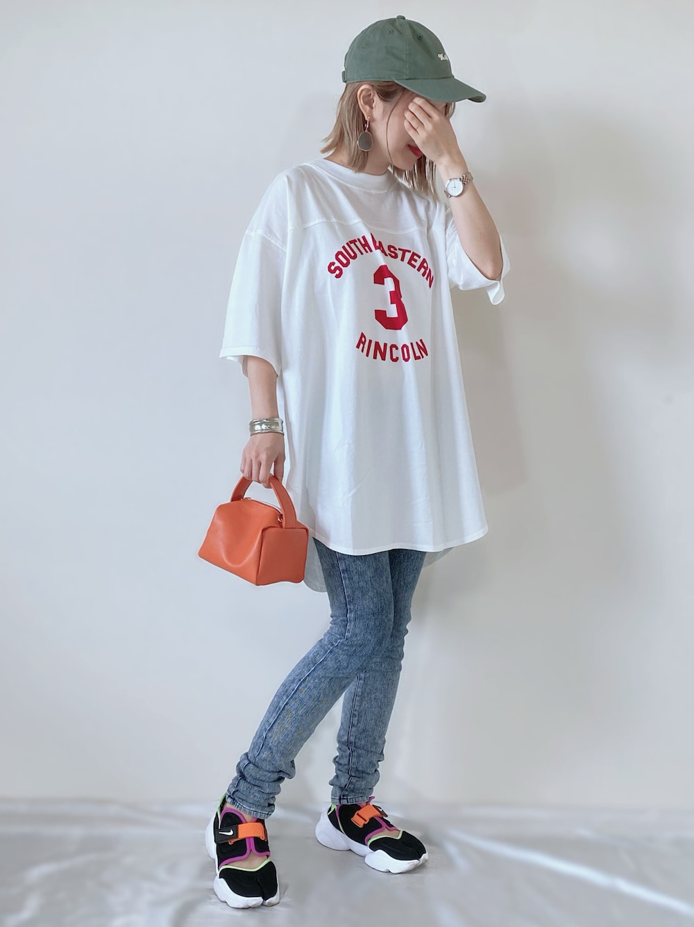 ホワイト系のTシャツ/カットソー、オレンジ系のバッグ、ブラック系のサンダルを着用したレディースの春コーディネートの1枚目の写真