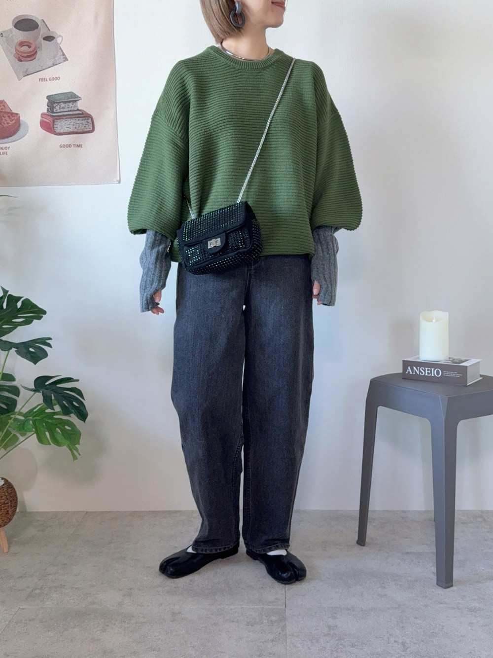 グリーン系のニット/セーター、ブラック系のデニムパンツ、ブラック系のクラッチバッグを着用したレディースの秋コーディネートの1枚目の写真