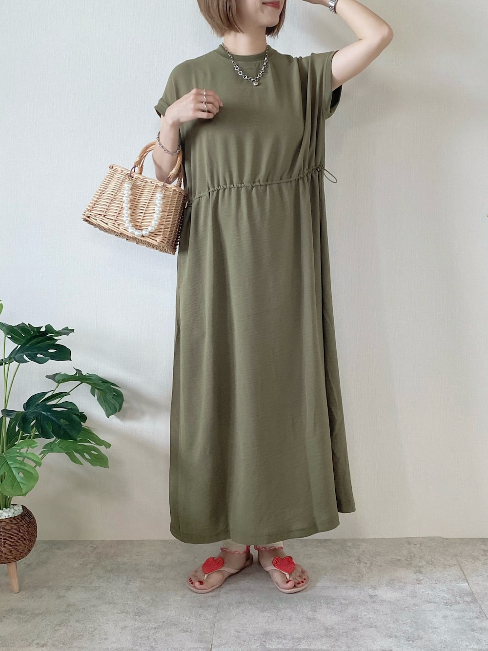 ベージュ系のかごバッグ、グリーン系のワンピース、ピンク系のサンダルを着用したレディースの夏コーディネートの1枚目の写真