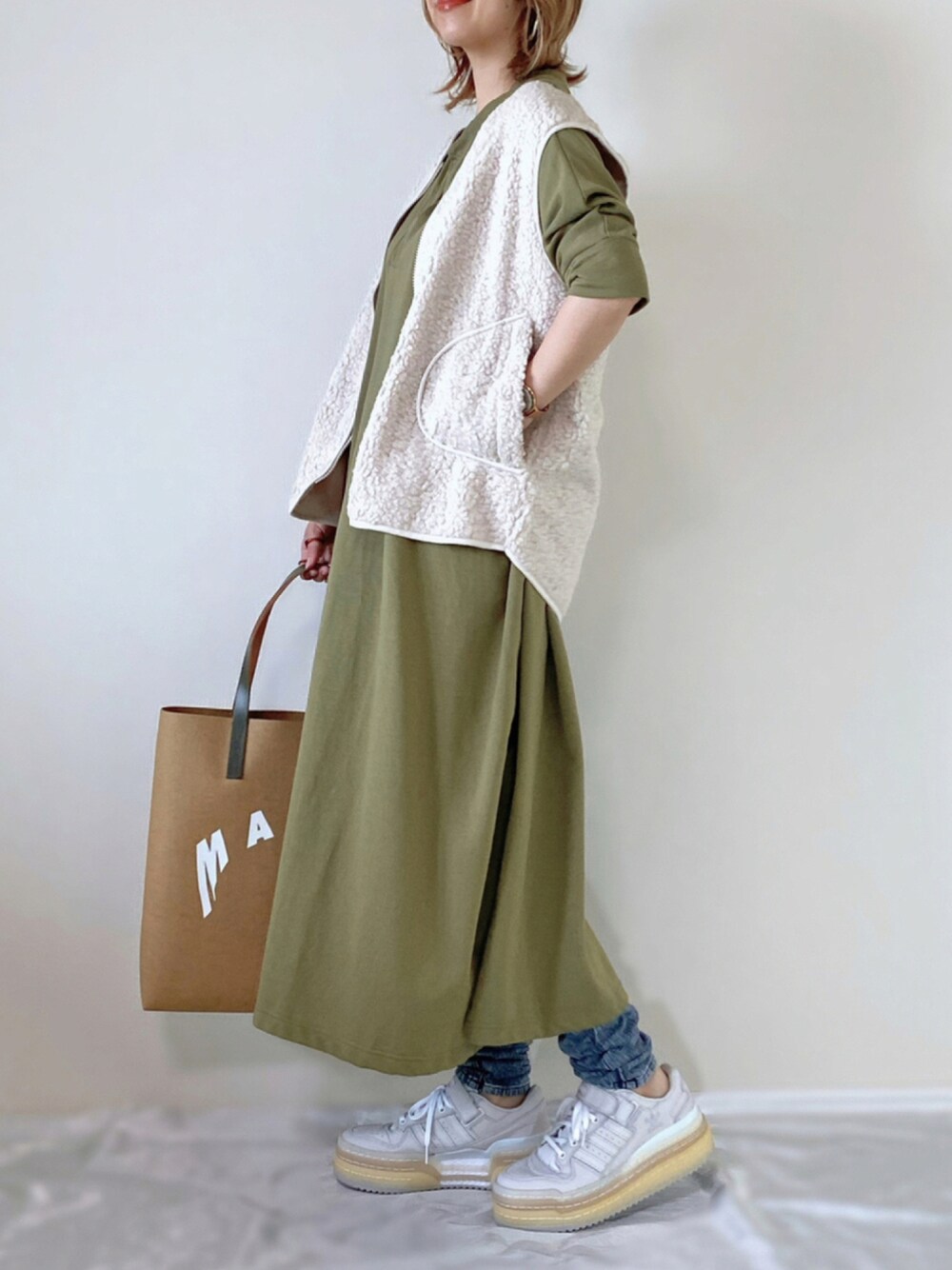 グリーン系のワンピース、ブラウン系のトートバッグ、ホワイト系のスニーカーを着用したレディースの秋コーディネートの1枚目の写真