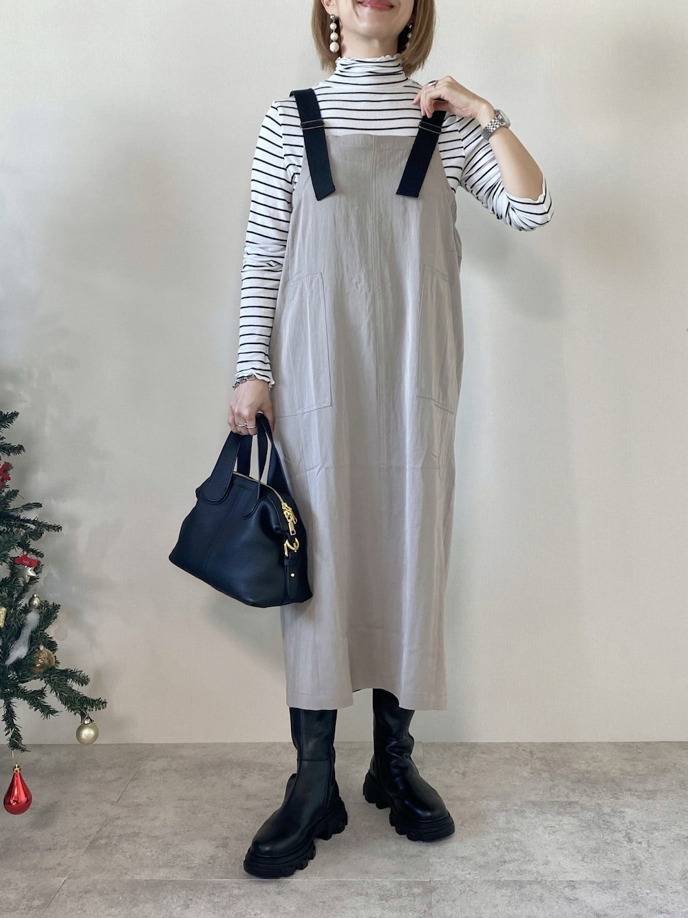 グレー系のジャンパースカート、ブラック系のバッグ、ホワイト系のTシャツ/カットソーを着用したレディースの冬コーディネートの1枚目の写真