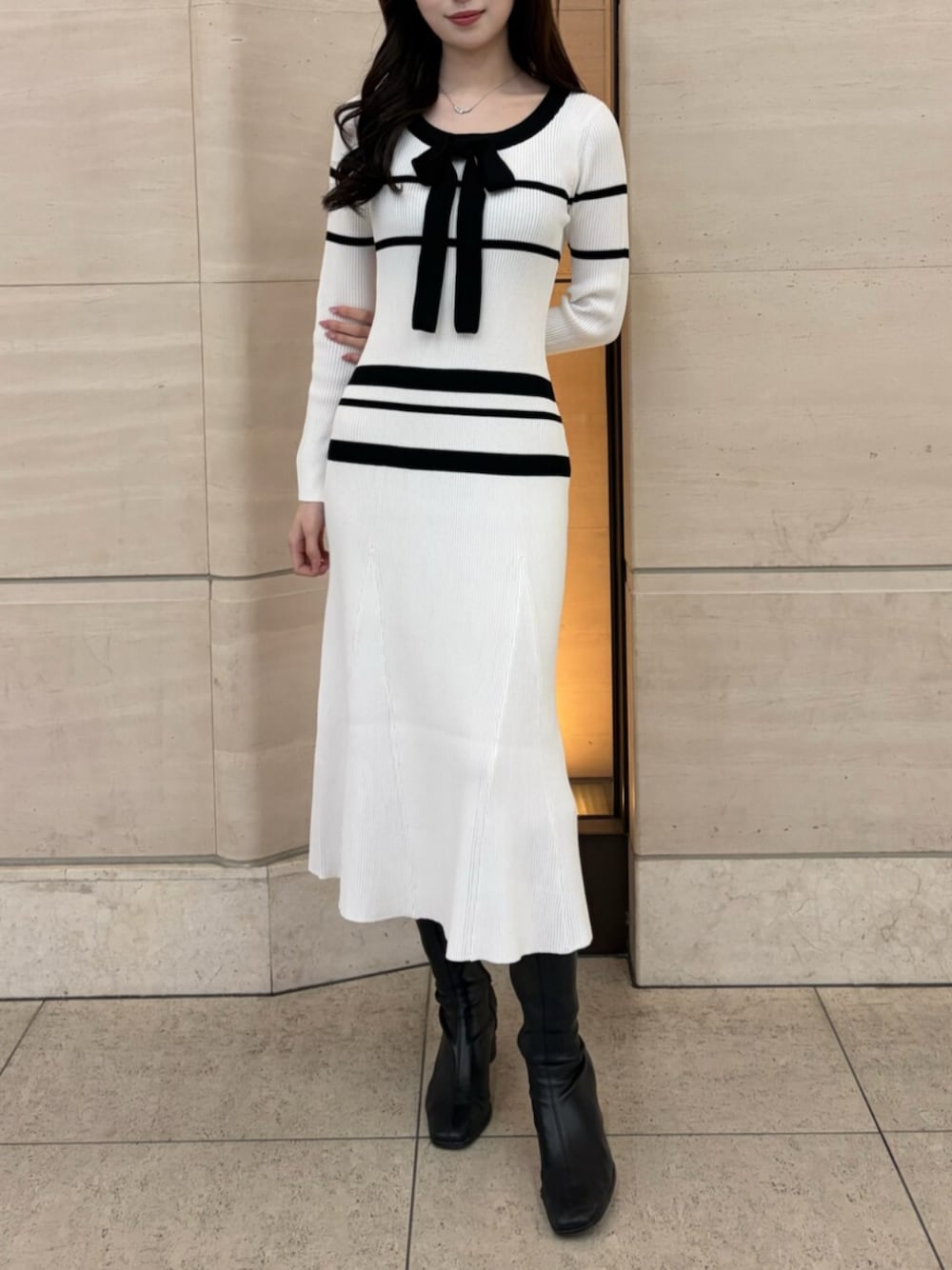 ホワイト系のワンピース、ブラック系のブーツを着用したレディースの冬コーディネートの1枚目の写真