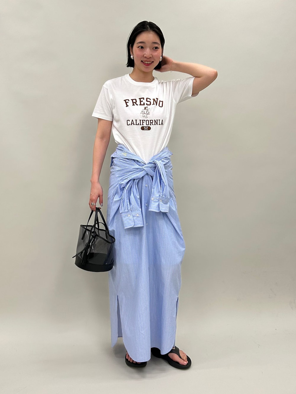 ブルー系のシャツワンピース、ホワイト系のTシャツ/カットソー、ブラック系のハンドバッグを着用したレディースの春コーディネートの1枚目の写真