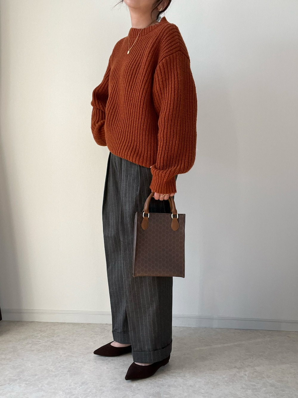 イエロー系のニット/セーター、ブラウン系のショルダーバッグ、ブラウン系のパンプスを着用したレディースの冬コーディネートの1枚目の写真