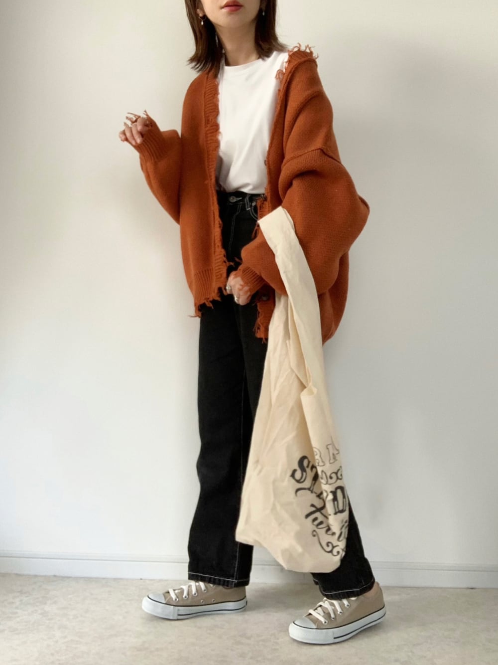 オレンジ系のカーディガン/ボレロ、ホワイト系のTシャツ/カットソー、ブラック系のデニムパンツを着用したレディースの秋コーディネートの1枚目の写真