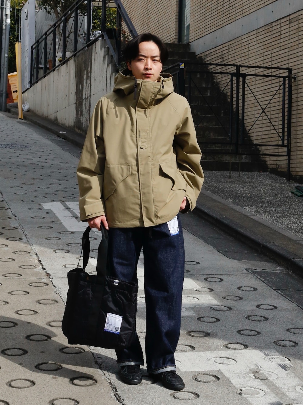 ベージュ系のマウンテンパーカー、ブルー系のデニムパンツ、ブラック系のショルダーバッグを着用したメンズの冬コーディネートの1枚目の写真