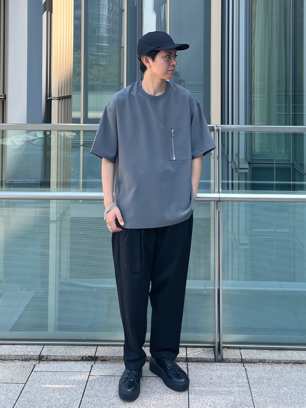 グレー系のTシャツ/カットソー、ブラック系のスラックス、ブラック系のスニーカーを着用したメンズの春コーディネートの1枚目の写真