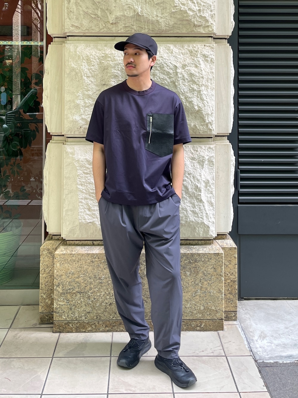 ブルー系のTシャツ/カットソー、グレー系のスラックス、ブラック系のキャップを着用したメンズの春コーディネートの1枚目の写真