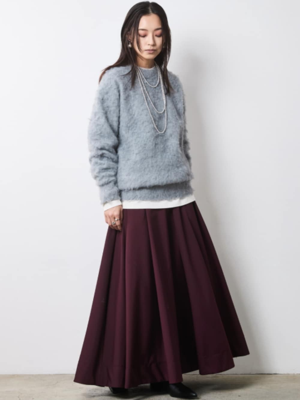 グレー系のニット/セーター、レッド系のスカートを着用したレディースの秋コーディネートの1枚目の写真
