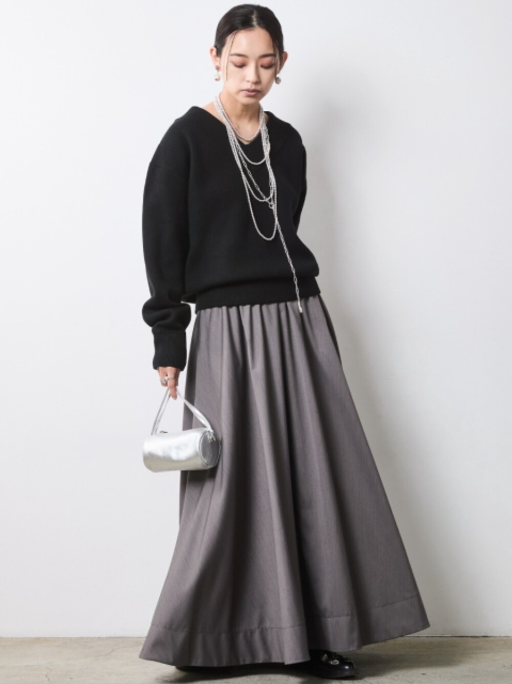 グレー系のスカート、ブラック系のニット/セーターを着用したレディースの秋コーディネートの1枚目の写真