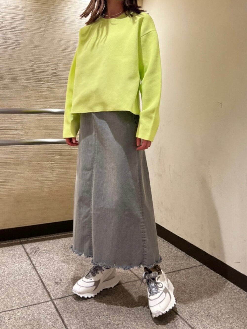 グレー系のデニムスカート、グリーン系のニット/セーター、ホワイト系のスニーカーを着用したレディースの春コーディネートの1枚目の写真