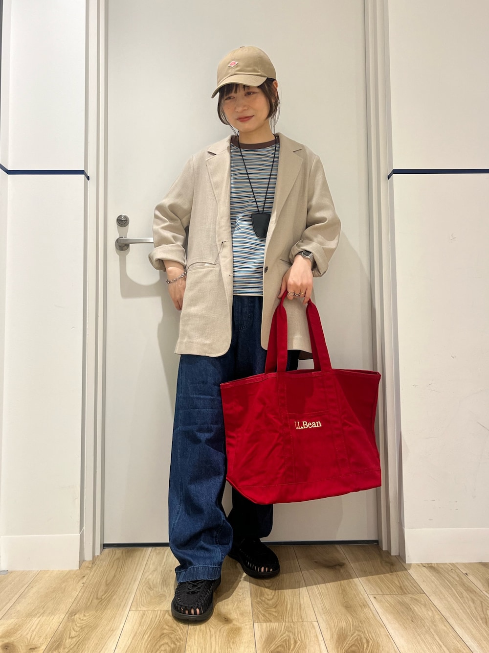 ブラック系のサンダル、ブルー系のデニムパンツ、レッド系のトートバッグを着用したレディースの春コーディネートの1枚目の写真