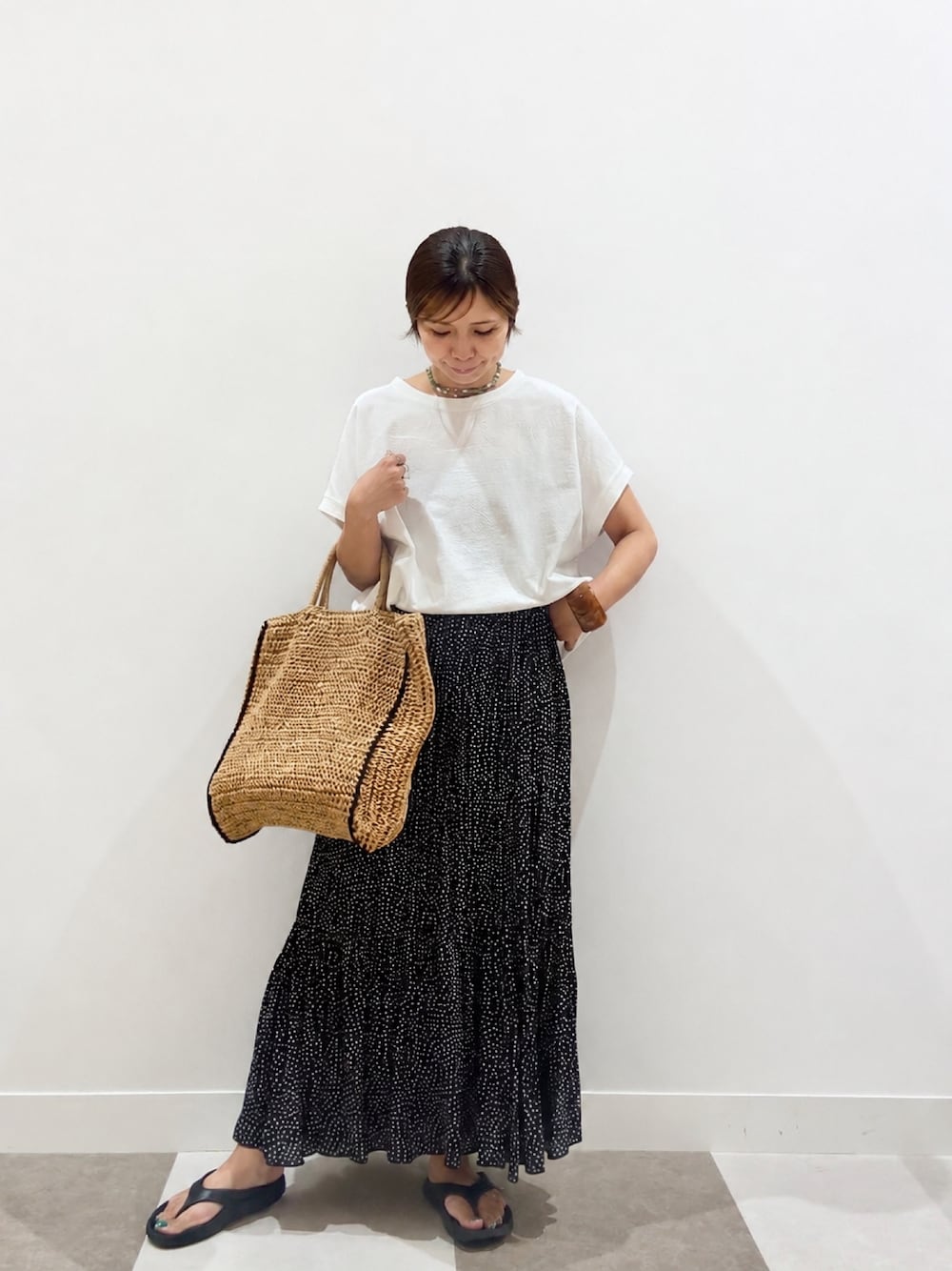ホワイト系のTシャツ/カットソー、ベージュ系のトートバッグ、ブラック系のスカートを着用したレディースの夏コーディネートの1枚目の写真