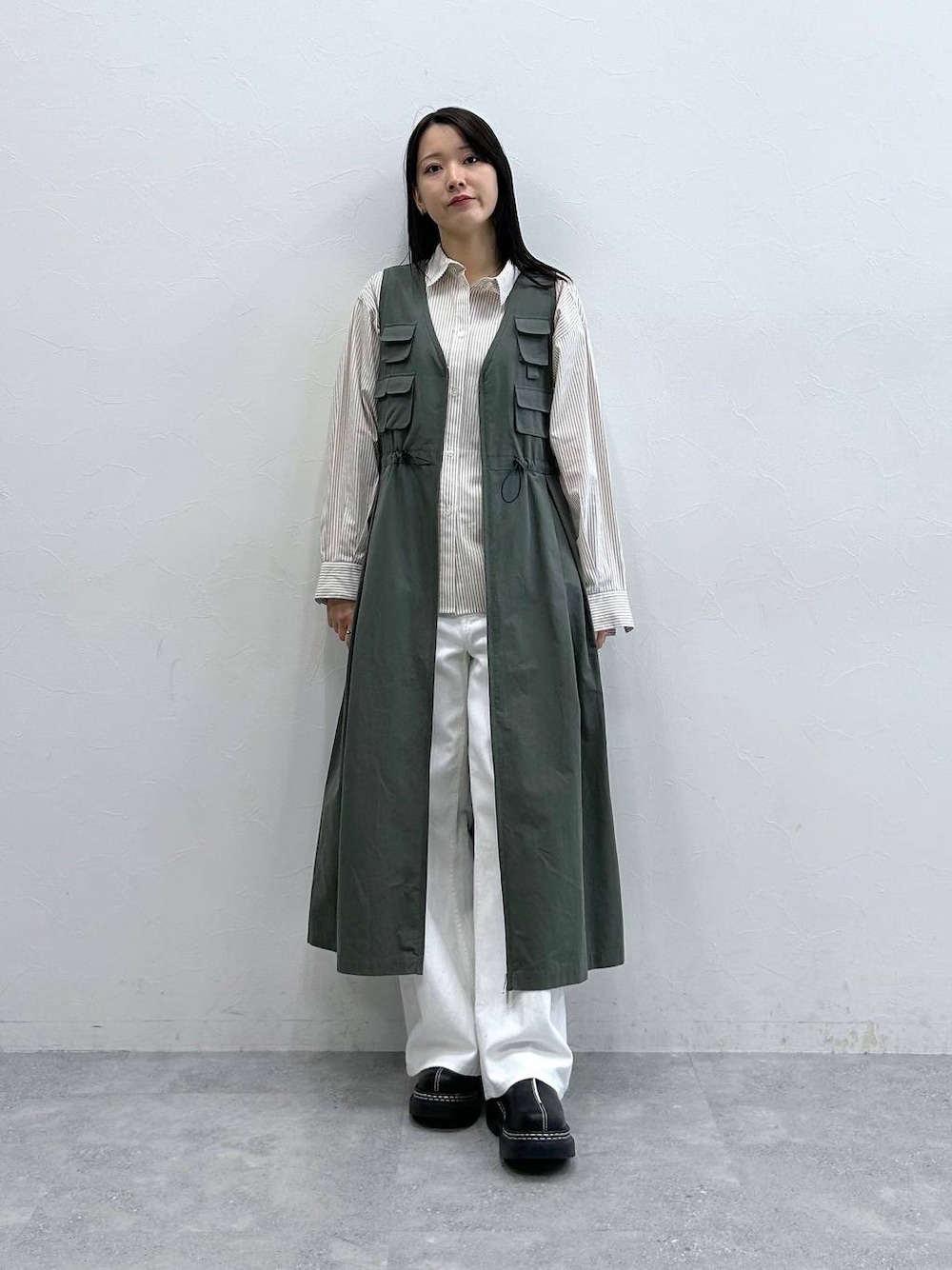 ブラック系のローファー、ホワイト系のデニムパンツ、グリーン系のジャンパースカートを着用したレディースの春コーディネートの1枚目の写真