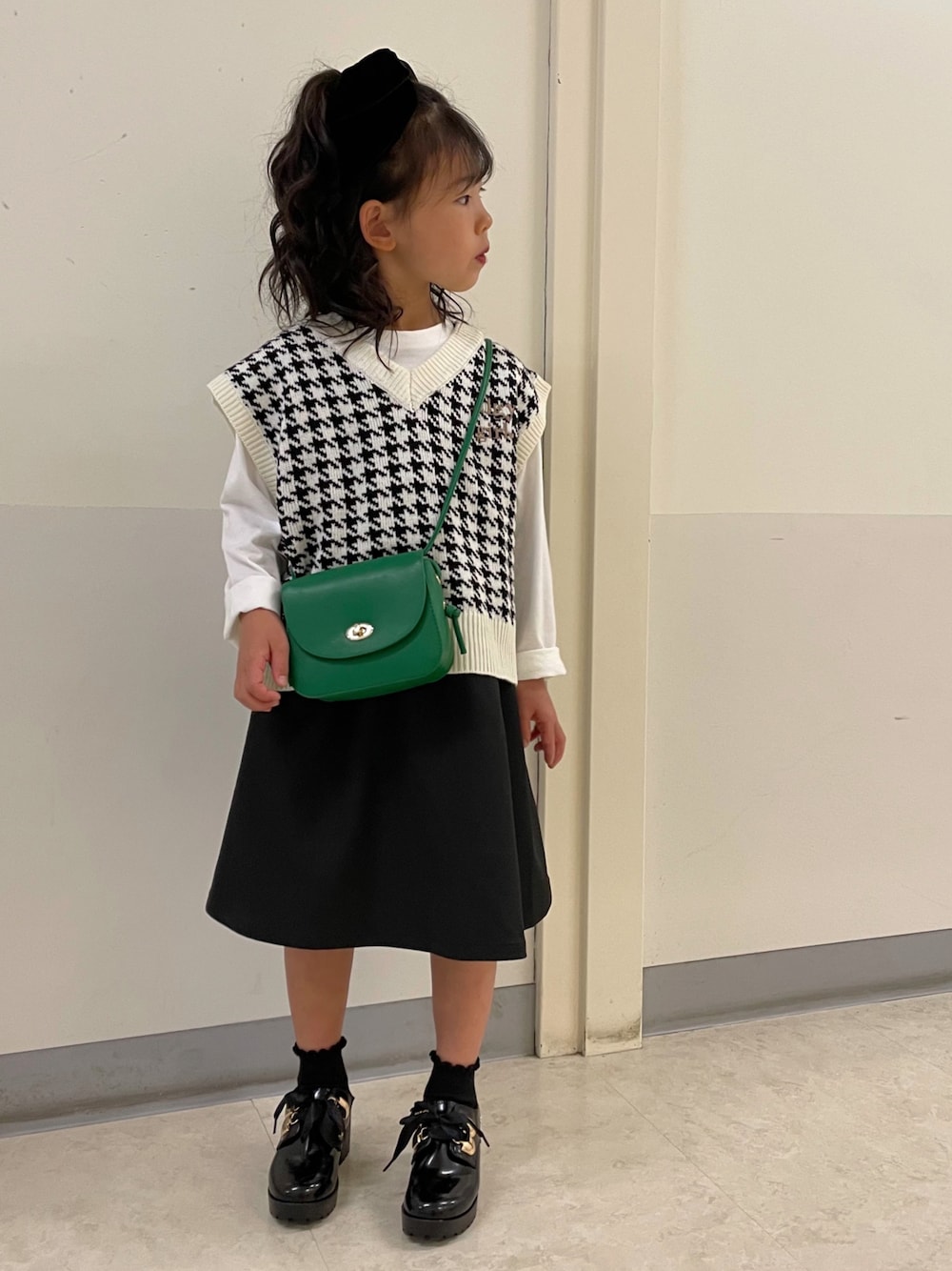 ベージュ系のベスト、ホワイト系のベスト、ブラック系のジャンパースカートを着用したキッズの秋コーディネートの1枚目の写真