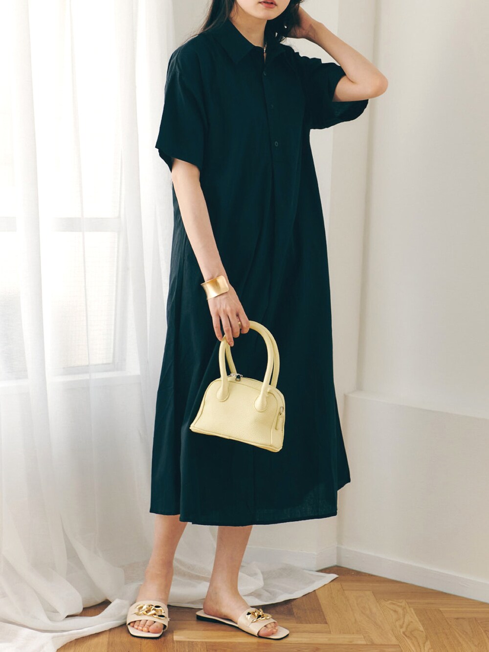 イエロー系のハンドバッグ、ブラック系のシャツワンピース、ホワイト系のサンダルを着用したレディースの春コーディネートの1枚目の写真