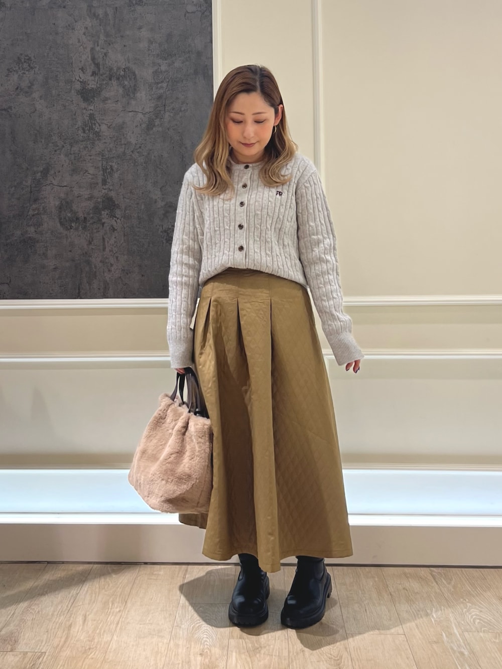 ベージュ系のショルダーバッグ、ブラウン系のスカート、グレー系のニット/セーターを着用したレディースの冬コーディネートの1枚目の写真